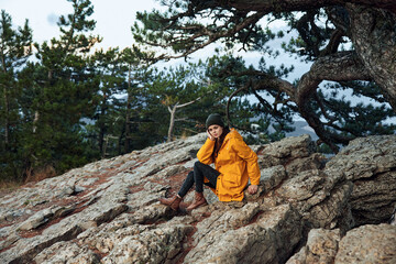 A woman in a stylish yellow coat enjoying a peaceful moment on a giant rock in the tranquil forest