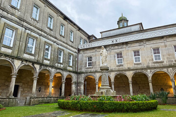 Interior facade of a stone church, a statue of Jesus Christ and the gardens of the inner courtyard wet by the rain