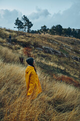 Fototapeta premium Lonely traveler in a vibrant yellow raincoat standing on a hill overlooking tall grasses and natural beauty