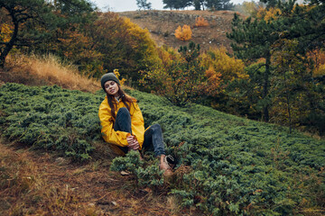 Woman relaxing on grassy hill in vibrant autumn forest, enjoying nature beauty and peaceful getaway from urban life