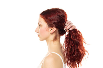 Fototapeta premium Profile of a young serious woman without makeup tying her long red wavy hair on a white studio background