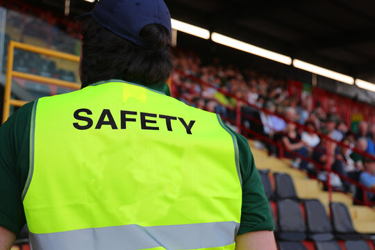 stadium security guard wearing a uniform with the word SAFETY standing among the spectators in the stands
