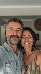 Fototapeta premium A man and woman smiling together taking a selfie in a room with a modern design featuring a ceiling fan and a round decorative item on the wall.