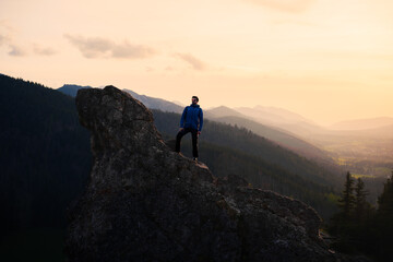 Man on rock in mountains at sunset, with clouds and sky in background