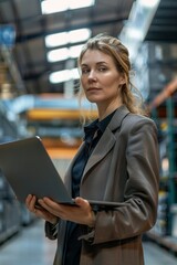 Fototapeta premium Businesswoman in a modern factory hall using laptop