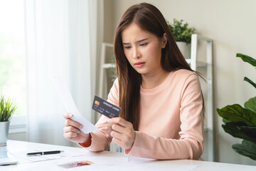 young asian woman holding credit card and invoice after stressed with monthly bill expenses and...
