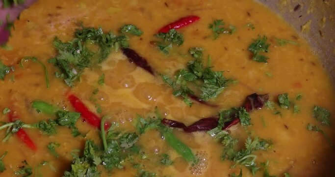 Adding boiling dal lentil into bagar tadka with deep fry tomato onion garlic cumin red dry chilli spice stair cooking dal ghotni whisk 