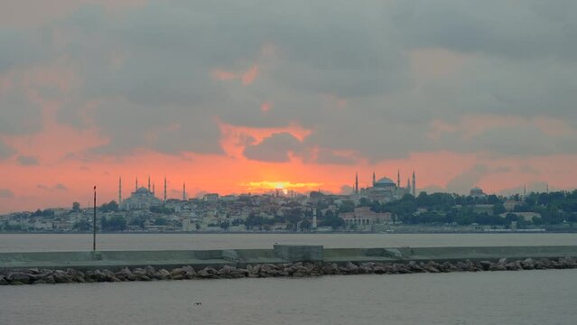 A majestic Istanbul sunset from a moving boat, highlighting the Aya Sophia, Blue Mosque, and Topkapi Palace against the fiery sky. Slowmotion video.