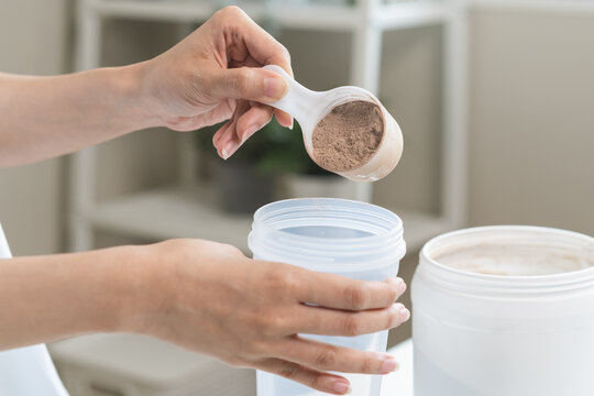 Diet meal replacement for weight loss, asian young woman in sportswear, hand in holding scoop making protein into bottle to shake, drink supplement for muscle after workout at home. Healthy body care.