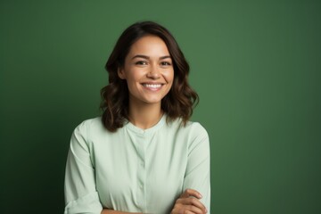 Fototapeta premium Portrait of a grinning woman in her 30s with arms crossed on pastel green background