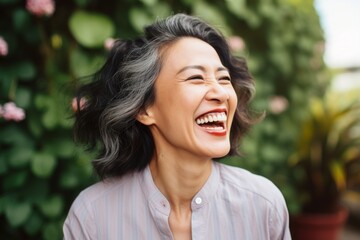 Portrait of a smiling asian woman in her 40s laughing while standing against pastel green background