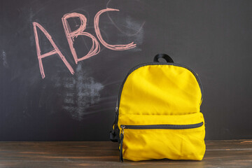 School bag on wooden desk in front of blackboard with English litters. Back to school concept.
