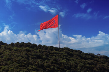 Turkish flag, on a red background white star and moon. Flag flies in the wind, public place.