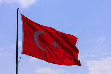 Turkish flag, on a red background white star and moon. Flag flies in the wind, public place.