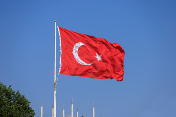 Turkish flag, on a red background white star and moon. Flag flies in the wind, public place.