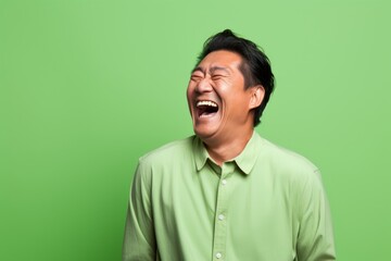 Fototapeta premium Portrait of a merry asian man in his 40s laughing on pastel green background