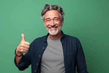 Portrait of a blissful man in his 50s showing a thumb up in front of pastel green background