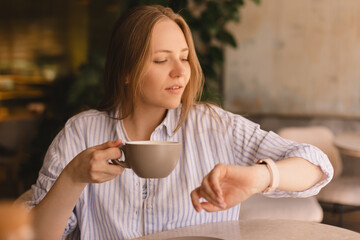 Portrait of gorgeous blonde smiling lady smelling, enjoying of coffee and drinking cappuccino from...