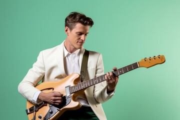 Portrait of a glad man in his 20s playing the guitar in pastel green background