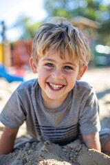 Smiling boy playing with sand on playground on sun