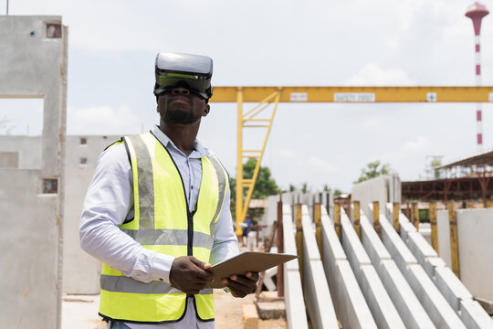 African American male construction engineer wearing virtual reality headset inspecting quality of structural at construction site. Male construction engineer working with VR headset at site work - Powered by Adobe