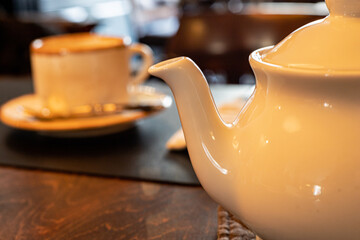 Teapot spout, close up of white teapot on served table, teacup on defocused café background....