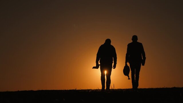 Father and his son walk through a field at sunset, carrying equipment for planting seedlings