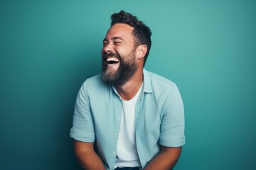 Fototapeta premium Portrait of a smiling man in his 30s laughing in front of pastel teal background
