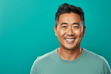 Portrait of a blissful asian man in his 40s smiling at the camera isolated on pastel teal background