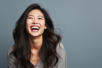 Fototapeta premium Portrait of a jovial asian woman in her 30s laughing in front of pastel gray background
