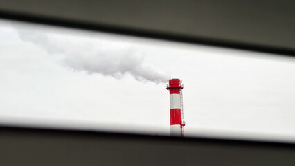 View through window blinds on renovated high industrial red and white chimney with metal stairs and...