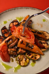 Fork with charred tomato slice over plate of grilled vegetables