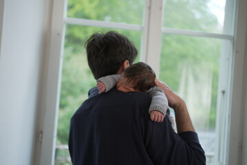 A father holds his newborn baby gently against his shoulder, capturing a serene and affectionate...