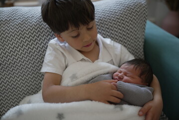 A heartwarming moment as an older brother cradles his newborn sibling, filled with tenderness and...