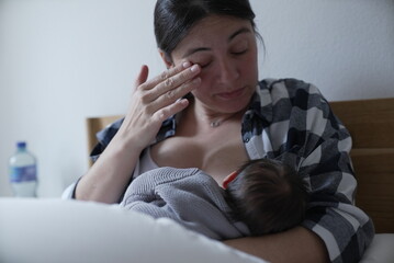 mother wipes away a tear while breastfeeding her baby, reflecting the emotional and tender aspects...