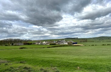 Obraz premium Verdant fields roll up to a quaint cluster of buildings, all under a brooding sky, heavy with grey clouds, signaling the imminent threat of a storm near Silsden, UK.
