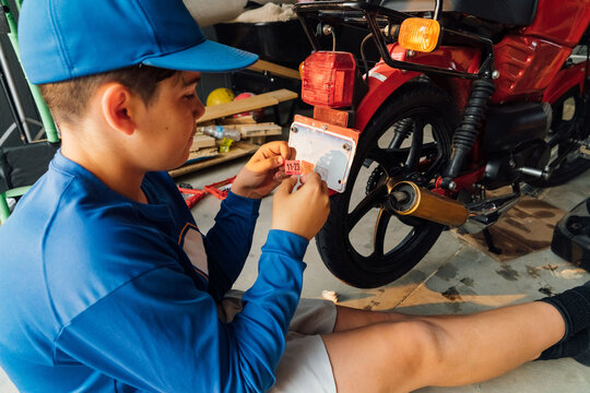 Teen boy applying tags to moped license plate. 