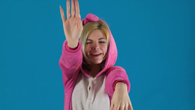 Teenager in pajamas dances moving hands on blue background. Young girl lets music guide fluid movements during performance
