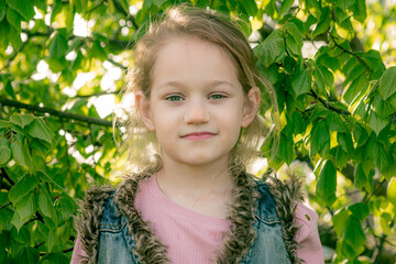 Portrait of a young girl with a gentle gaze, surrounded by lush green leaves, highlighted by soft sunlight.