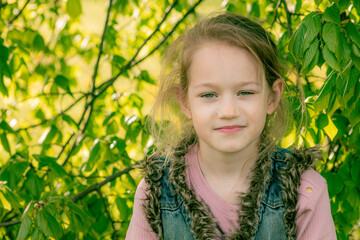 Portrait of a young girl with a gentle gaze, surrounded by lush green leaves, highlighted by soft sunlight.