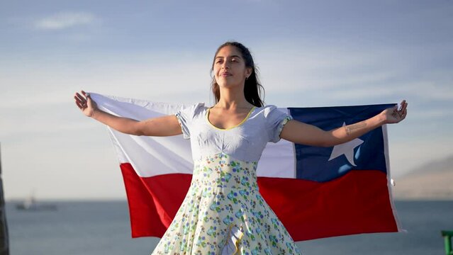 portrait beautiful chilean woman holding a flag of Chile wearing national costume outdoors against blue sky, celebration and patriotism concept	