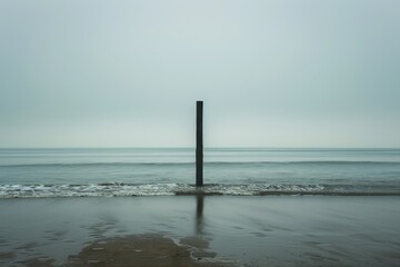 A pole stands tall in the water on a foggy day, surrounded by mist and a calm sea