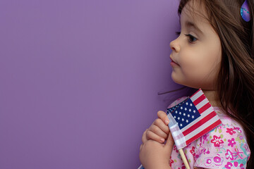 Little girl holding a USA flag to her chest, close-up side view on violet background.