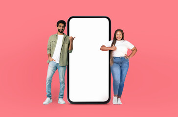 Positive multiethnic man and a woman are standing next to a giant phone, appearing to be engaged in...