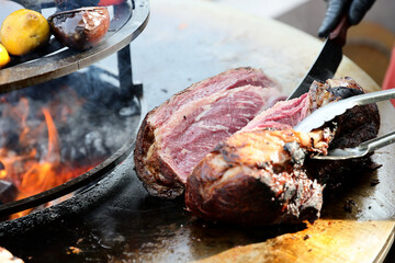 A large pieces of raw fresh steak are grilling on flaming grill.