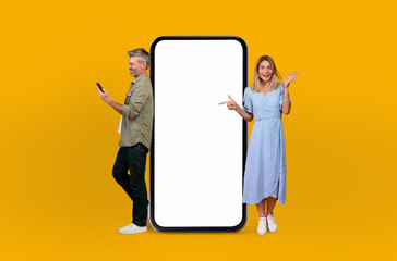 Mature man and woman are standing together next to a huge telephone, appearing to be engaged in a...