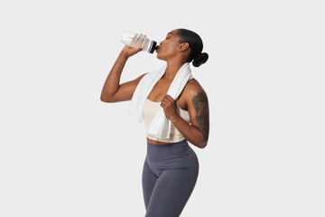 African American woman in sportswear holding a plastic bottle to her lips, drinking water isolated...