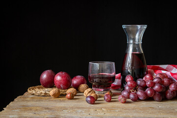 View of rustic bottle, glass with red wine, cloth, grapes, plums and nuts on wooden table, black...