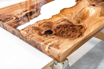 Live edge elm burl slab table top with central epoxy resin river on sawhorses in professional...