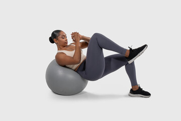 A focused young black woman engages in a core workout, employing a fitness ball to perform an advanced abdominal exercise designed to improve strength and stability.
